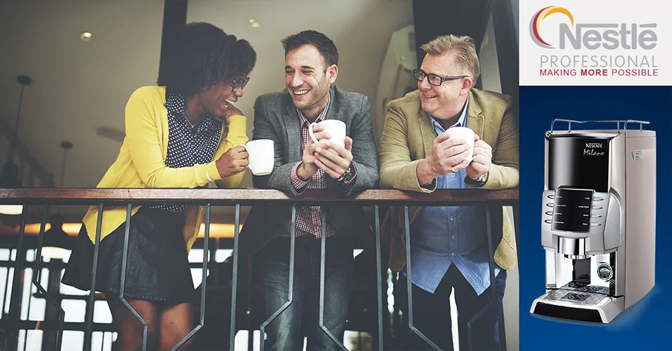 3 colleagues in the workplace chatting and drinking coffee with the Nescafé Milano machine in focus.