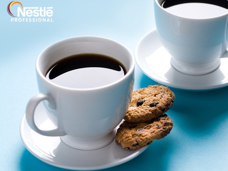 Two cups of black coffee with chocolate chip cookies on white saucers