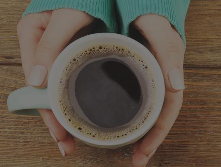 A woman warming her hands on a hot cup of Nescafé Ricoffy coffee.