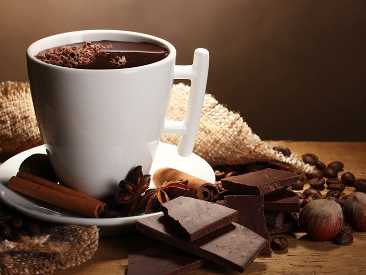 A cup with Nestlé Hot Cholocate with cinnamon sticks and chocolate pieces on the side.
