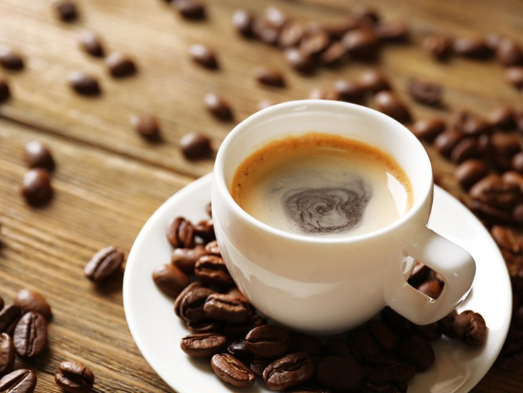 A coffee cup with Nesacfé Ricoffy and coffee beans scattered next to it on the table.