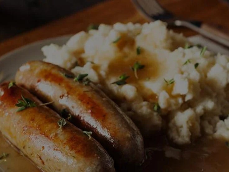 A dish with Maggi mash potatoes and sausages on the side.