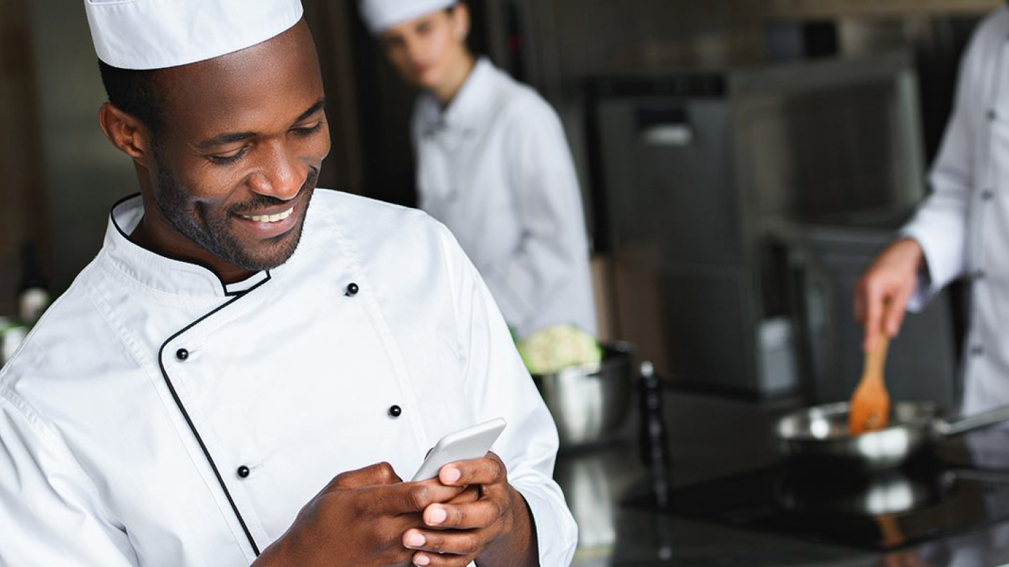 A chef in a kitchen using his phone to contact.