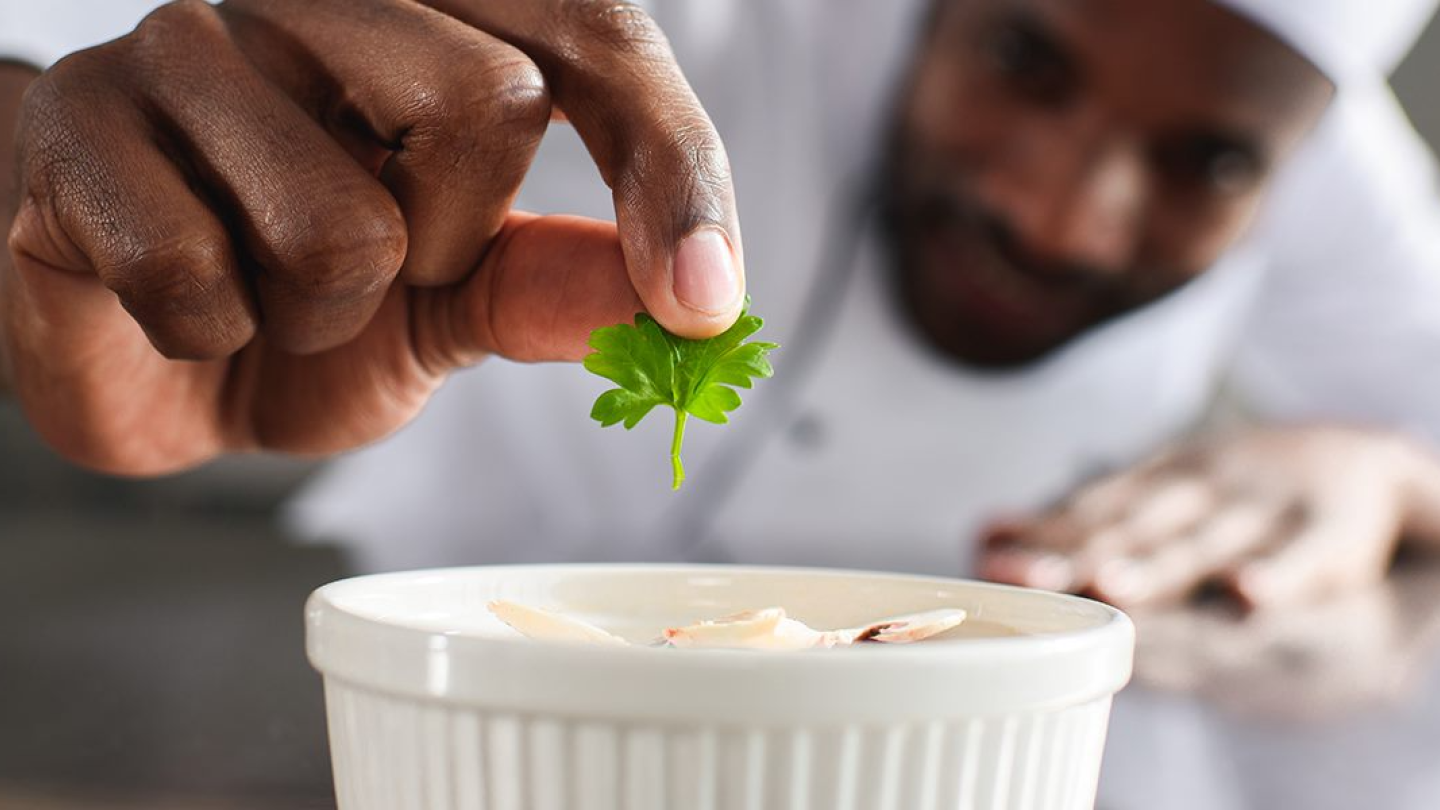 A chef adding herbs leaves in a dessert bowl.
