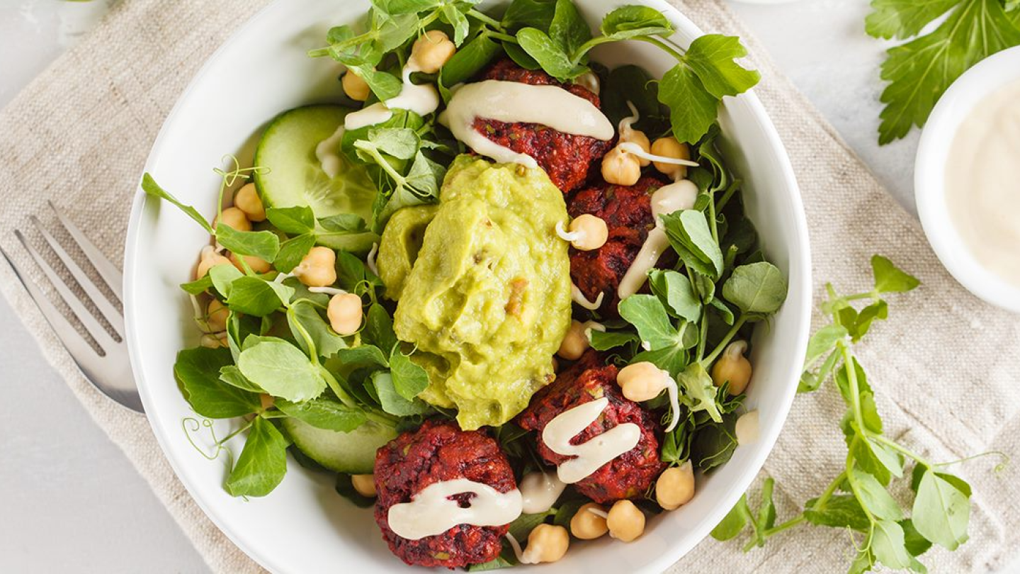 A plate with a salad of cucumber, chickpeas, herbs, guacamole and other ingredients.